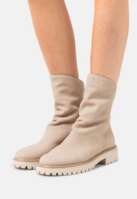 Beige kožené kotníkové boty s volným designem, kulatou špičkou a robustními bílými gumovými podrážkami s drážkami pro lepší trakci.