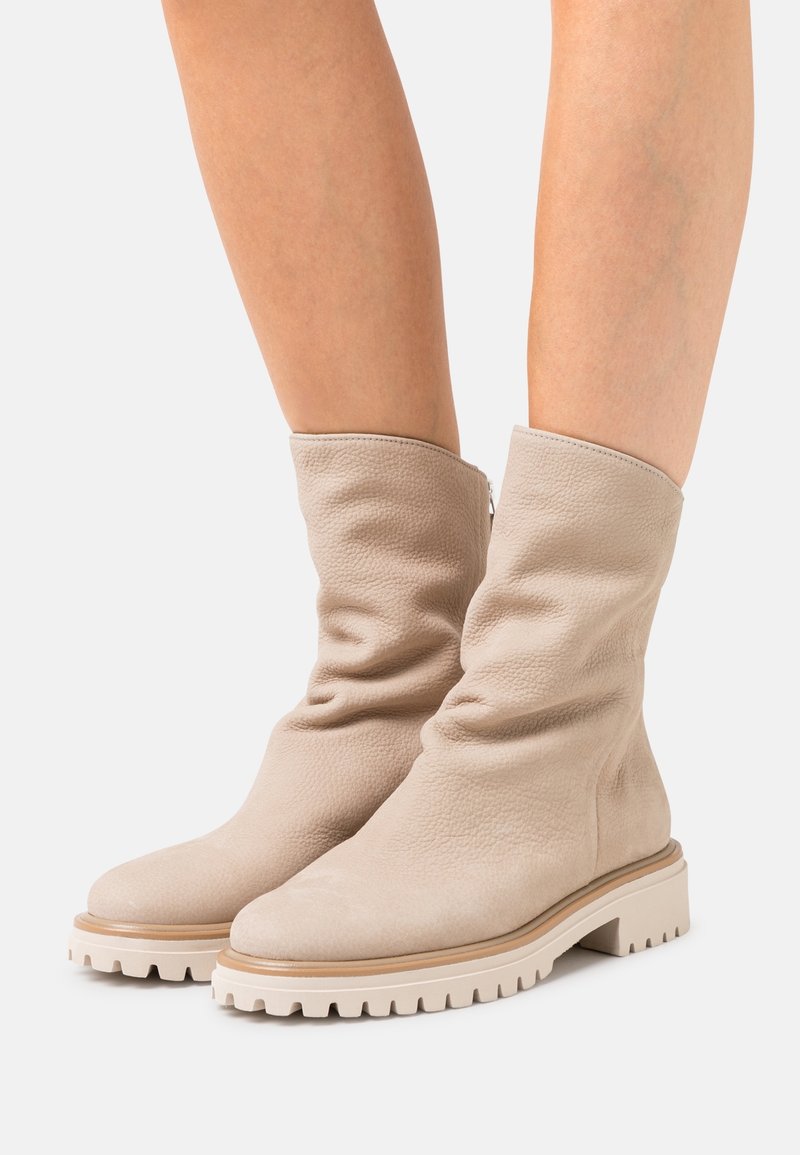 Beige kožené kotníkové boty s volným designem, kulatou špičkou a robustními bílými gumovými podrážkami s drážkami pro lepší trakci.