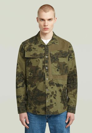 Grønne camouflage knap-op skjorte med to brystlommer, lange ærmer og en lige kant. Lavet af stof i varierende nuancer af grøn og brun.