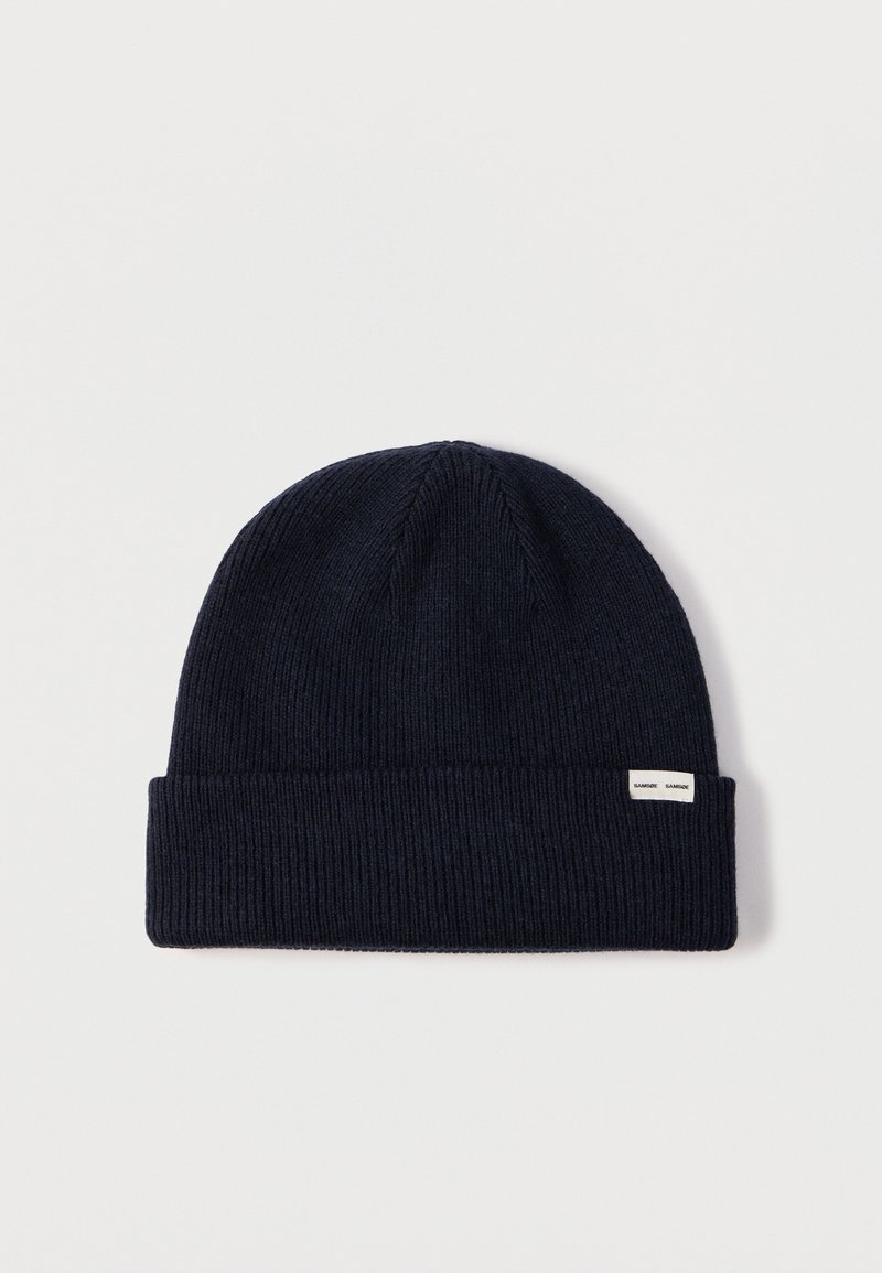 Tumši zila adīta cepure ar salocītu aproci, sānā ar nelielu etiķeti. Visa cepures virsma ir ribota.