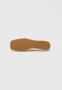 Semelle de chaussure beige texturée avec une empreinte à motifs circulaires et un accent en caoutchouc marron. Forme plate et rectangulaire.