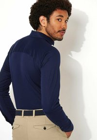 Donkerblauw poloshirt met lange mouwen en een kraag, voorzien van een gestructureerde achterkant, gecombineerd met lichtbeige broeken en een geweven riem.