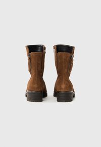 Braune Wildleder-Ankle-Boots mit schwarzen Lederelementen, Reißverschluss und strukturierten Absätzen. Mit leicht rund zulaufender Spitze und gestickten Details.