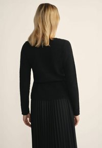 Czarny, puszysty sweter z długimi rękawami, dopasowaną talią i dekoltem w kształcie litery V, połączony z plisowaną czarną spódnicą, ukazującą teksturowany wygląd.