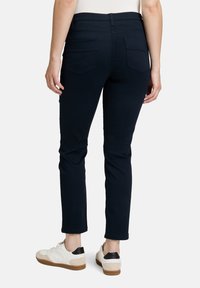 Tummansiniset istuvat housut, joissa on keskipitkä vyötärö ja kaksi takataskua, yhdistettynä valkoisiin ja ruskeisiin lenkkareihin. Sileä rakenne.