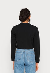 Veste noire courte au design simple et à manches longues, associée à un jean en denim clair taille haute avec des poches arrière.