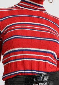 Czerwony sweter z golfem w prążki z poziomymi pasami w białym i niebieskim kolorze. Posiada dopasowany krój i teksturowany materiał, połączony z czarnym paskiem.
