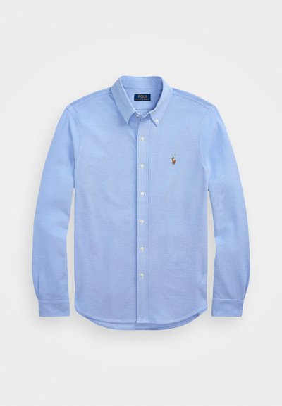 Svetlo modra srajca z dolgimi rokavi in gumbi, narejena iz mehke bombažne tkanine, ima klasičen ovratnik in majhen vezen logotip na prsih.