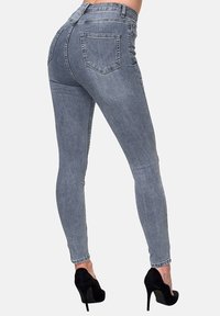 Jeans ajustados de denim gris claro, con cintura alta, dos bolsillos traseros y una textura suave. Combinados con zapatos de tacón negro.