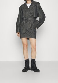 Giacca corta in finta pelle nera con vita cintrata, abbinata a una gonna di jeans nera e stivali militari neri lucidi con lacci.