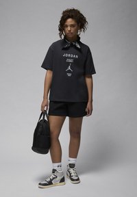 Black Jordan graphic t-shirt with oversized fit, paired with black shorts. Accessories include a black backpack and high-top sneakers with light accents.