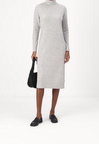 Robe en maille côtelée gris clair avec un col montant et des manches longues, associée à un sac tressé noir et des mocassins noirs. Silhouette simple et droite.