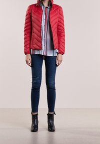 Rode gewatteerde jas met hoge kraag, gecombineerd met een verticaal gestreept shirt, donkere jeans en zwarte enkellaarsjes. Gladde textuur en aansluitend ontwerp.