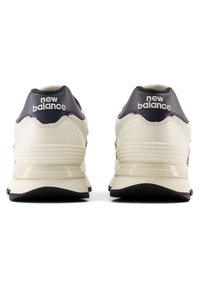 Vita och marinblå löparskor med en mjuk läderöverdel, lagerdesign och gummisula. "New Balance"-logga visad på hälen.