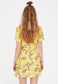 Robe jaune à fleurs avec manches courtes et jupe évasée. Présente des motifs floraux bleus et roses sur un fond jaune.