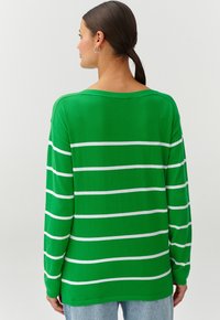 Grüner gestrickter Pullover mit weißen horizontalen Streifen, entspannt geschnitten, mit weitem Ausschnitt und langen Ärmeln. Weiche Textur und mittellange Passform.