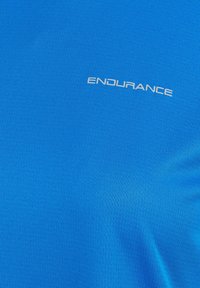 Sininen urheilupaita, jossa on teksturoitu kangas. "ENDURANCE"-logo valkoisena rinnan kohdalla, esittelee istuvaa muotoilua.