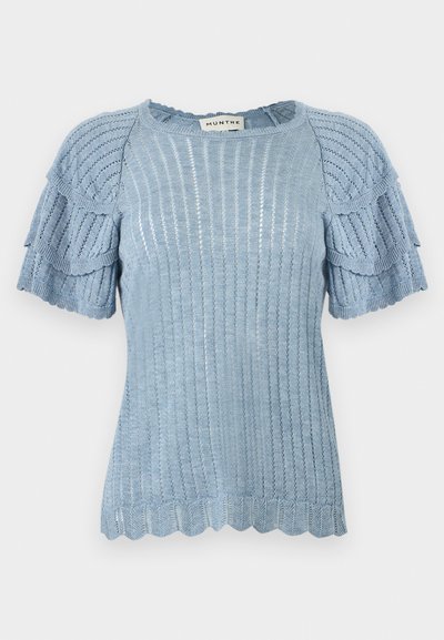 Haut tricoté bleu clair avec manches courtes à volants, texture côtelée et ourlet festonné. L'étiquette porte la mention "MUNTHE."