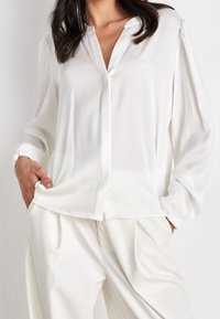 Weiße Bluse mit langen Ärmeln, Kragen, durchgehender Knopfleiste und weichem, glattem Stoff. Mit leicht gepufften Ärmeln und lockerer Passform.