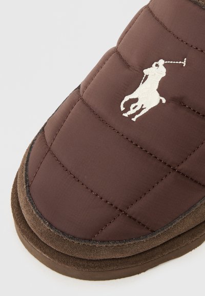 Hnědá prošívaná papuče s nubukovým spodkem, zdobená bílým vyšitým logem polo hráče. Měkká textura a zaoblený tvar pro pohodlí.