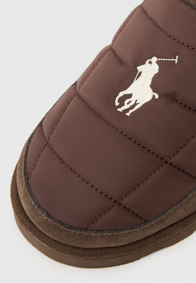 Braune gesteppte Hausschuhe mit einer Wildleder-Unterseite, die ein weißes gesticktes Polo-Spieler-Logo tragen. Weicher Stoff und runde Form für zusätzlichen Komfort.