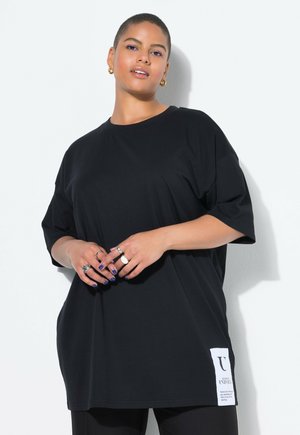 Black oversized t-shirt made of cotton, featuring short sleeves and a side tag with white text. Smooth texture, relaxed fit, and simple design.