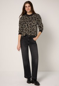Maglione grigio con stampa leopardata, polsini e scollo a costine, abbinato a jeans neri a gamba larga e stivali neri alla caviglia. Sfondo chiaro uniforme.