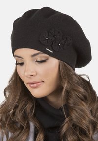 Černý pletený baret se třemi květinovými akcenty z textilu a malým stříbrným logem. Design je měkký s volným a uvolněným střihem.