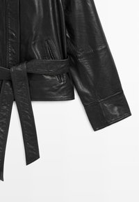 Černá kožená bunda s opaskem v pase, má boční kapsy a hladkou texturu, prezentující minimalistický design s přizpůsobenými rukávy.