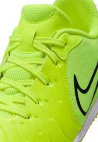 Zapatilla deportiva de color amarillo neón con parte superior de malla, material sintético texturizado y logotipo Swoosh negro. El diseño incluye cordones redondos y lengüeta acolchada.