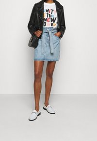 Jeanskjol med bälte i midjan, ihop med en svart läderjacka och en t-shirt med grafik. Skorna är vita loafers med kedjedetalj.