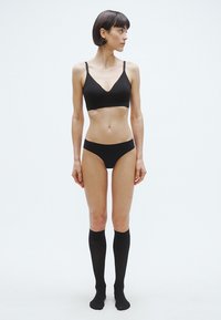 Sort bralette med justerbare stropper, matchende sorte trusser og knælange sorte sokker. Stoffet ser glat ud, med få sømme og et enkelt design.