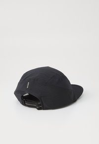 Svart caps med buet skygge, laget av lettvektig stoff med et teksturert mønster og perforerte seksjoner for pusteevne. Justerbar stropp bak.