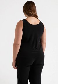 Top negro sin mangas con escote redondeado, elaborado en una tela suave. La parte trasera presenta un diseño sin costuras, combinado con pantalones negros.