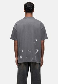 Szary, rozmiar oversize T-shirt wykonany z bawełny, z postarzonymi, białymi plamami farby oraz krótkimi rękawami; luźny krój z okrągłym dekoltem.