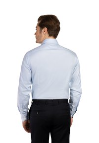 Himmelblaues Hemd mit glatter Textur, langen Ärmeln und klassischem Kragen, kombiniert mit dunklen Hosen, die über einen Knopf und Taschendetails verfügen.