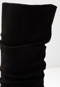 Czarne zamszowe kozaki sięgające do kolan o luźnym fasonie, z miękką teksturą i subtelnymi fałdami. Brak widocznych elementów metalowych lub ozdobnych.