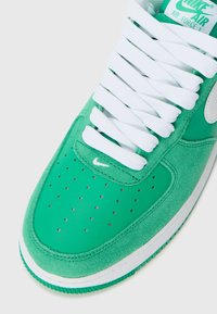 Green suede and leather sneaker with white laces, perforated toe box, and blue accents, featuring a visible Nike logo on the side.