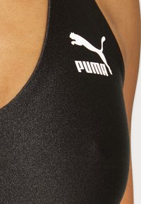 Top deportivo negro con una textura elegante y suave. Presenta un logo de Puma blanco en la parte superior izquierda, realzado por un escote bajo.