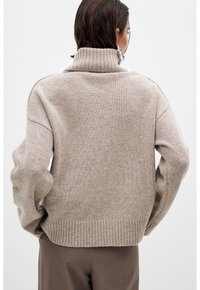 Beige knit sweater with a high ribbed collar, dropped shoulders, and ribbed hem. Soft texture, slightly loose fit, plain design.