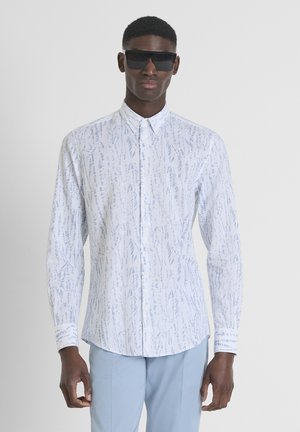Witte overhemd met knopen, featuring een blauw abstract patroon, lange mouwen en een gebogen zoom. Gemaakt met zwarte zonnebril en lichtblauwe broek.