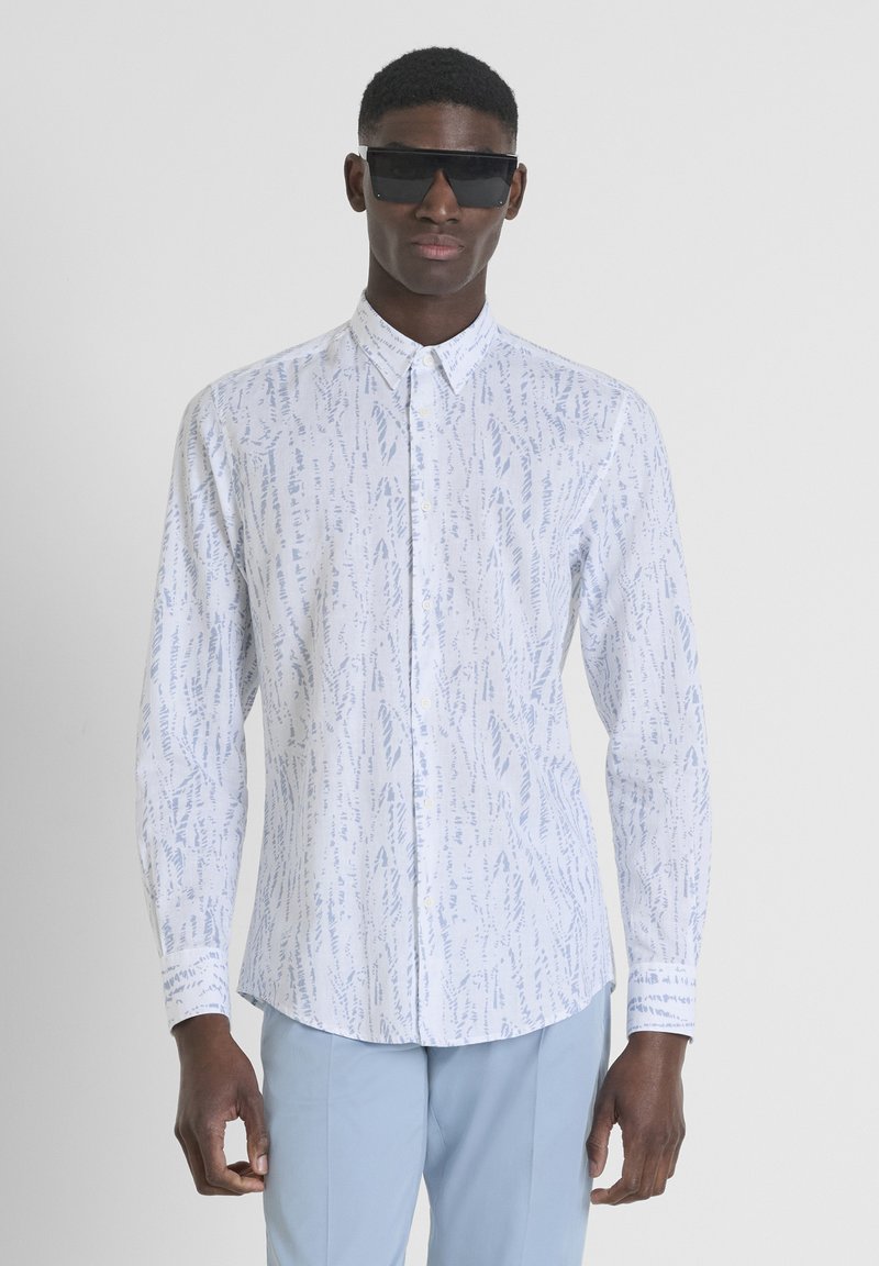 Witte overhemd met knopen, featuring een blauw abstract patroon, lange mouwen en een gebogen zoom. Gemaakt met zwarte zonnebril en lichtblauwe broek.