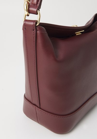 Borsa a mano in pelle bordeaux con texture liscia, forma strutturata, hardware dorato e base arrotondata. Presenta una chiusura superiore.