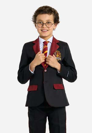 Blazer nero con dettagli bordeaux, camicia bianca e cravatta a righe rosse e gialle. Presenta un logo di Gryffindor e pantaloni abbinati con rifiniture.