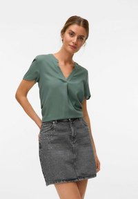 Haut vert à manches courtes avec un décolleté en v, associé à une jupe en denim grise avec des accents cloutés sur le côté gauche.