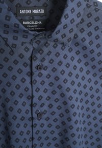 Camicia a maniche corte di colore blu navy con un motivo geometrico in tonalità scure, dotata di colletto classico e chiusura a bottoni, realizzata in cotone stampato misto.