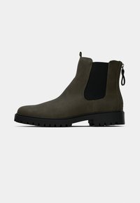 Olivgrüner Leder-Chelsea-Stiefel mit schwarzen elastischen Seitenpanneln, einer Zuglasche und einer dicken schwarzen Gummisohle mit einem robusten Profil.