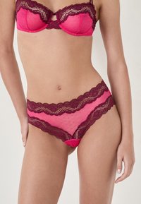 BH und Slip-Set in leuchtendem Pink und burgunderfarbenem Spitze. Der BH hat gepolsterte Cups, Spitzenverzierungen und verstellbare Träger. Der Slip hat florale Spitzenakzente.