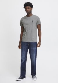 Grå bomulds t-shirt med et lille grafisk tryk på brystet, parret med mørkebl å denim jeans og sorte sneakers med hvide detaljer.