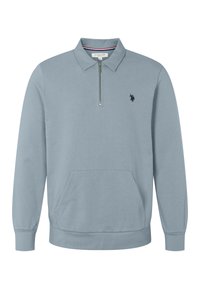 Svetlo modrý pulover s dlhým rukávom a golierom, polovičný zips vpredu, klokaní vrecko a malé tmavé vyšívané logo koňa na ľavej hrudi.